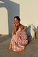 Pink Sun Anais Dress with iconic soleil motifs and gold flecks, shown on a model crouching by white vases.