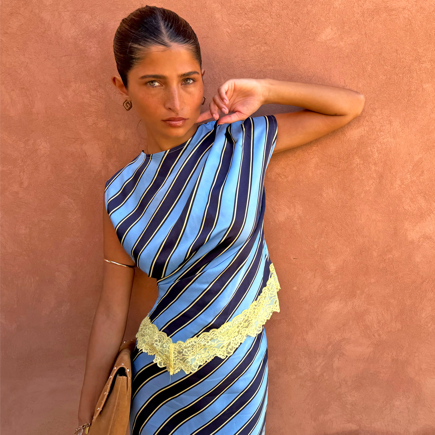 Stripe A-Symmetrical Top in blue diagonal print with yellow lace trim, shown against a terracotta wall.