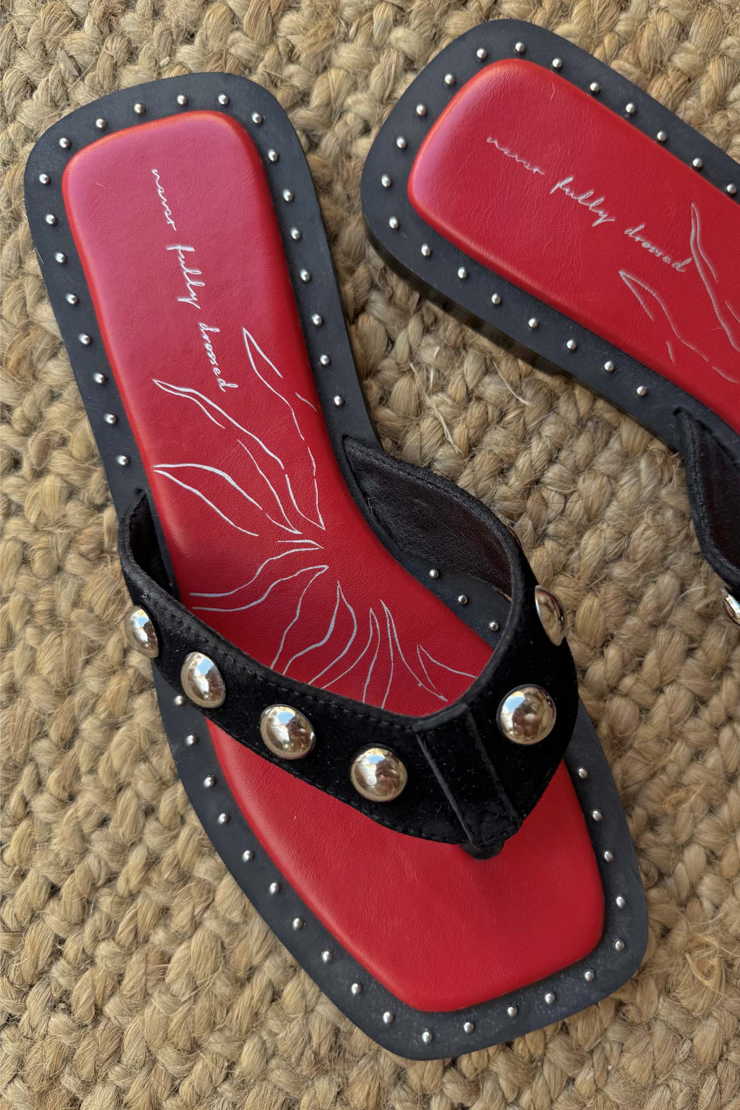 Black Leather Stud Sandals with silver studs, a square toe and a red graphic footbed on a woven mat.