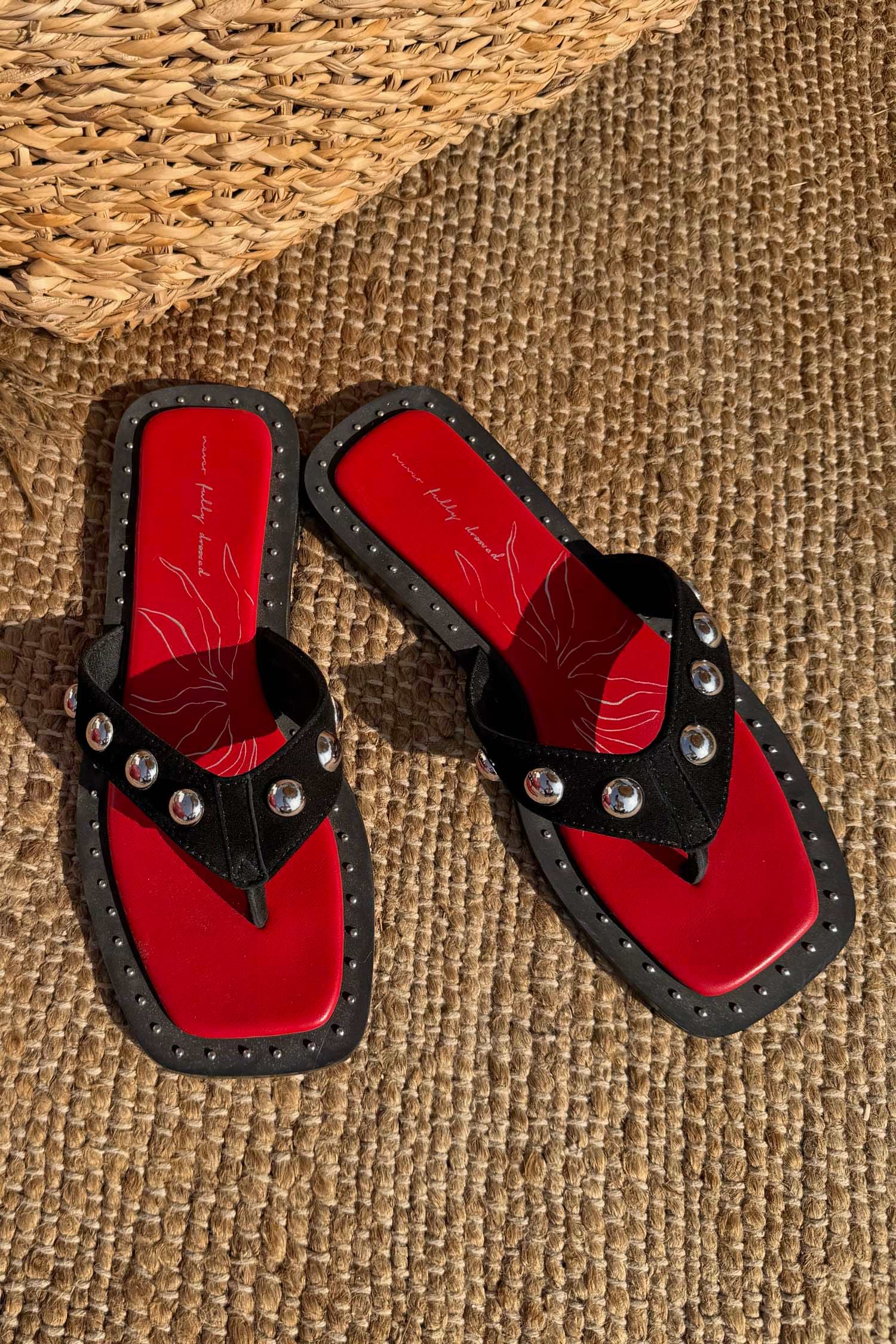 Black Leather Stud Sandals with silver studs and a red square-toe footbed on a woven mat.