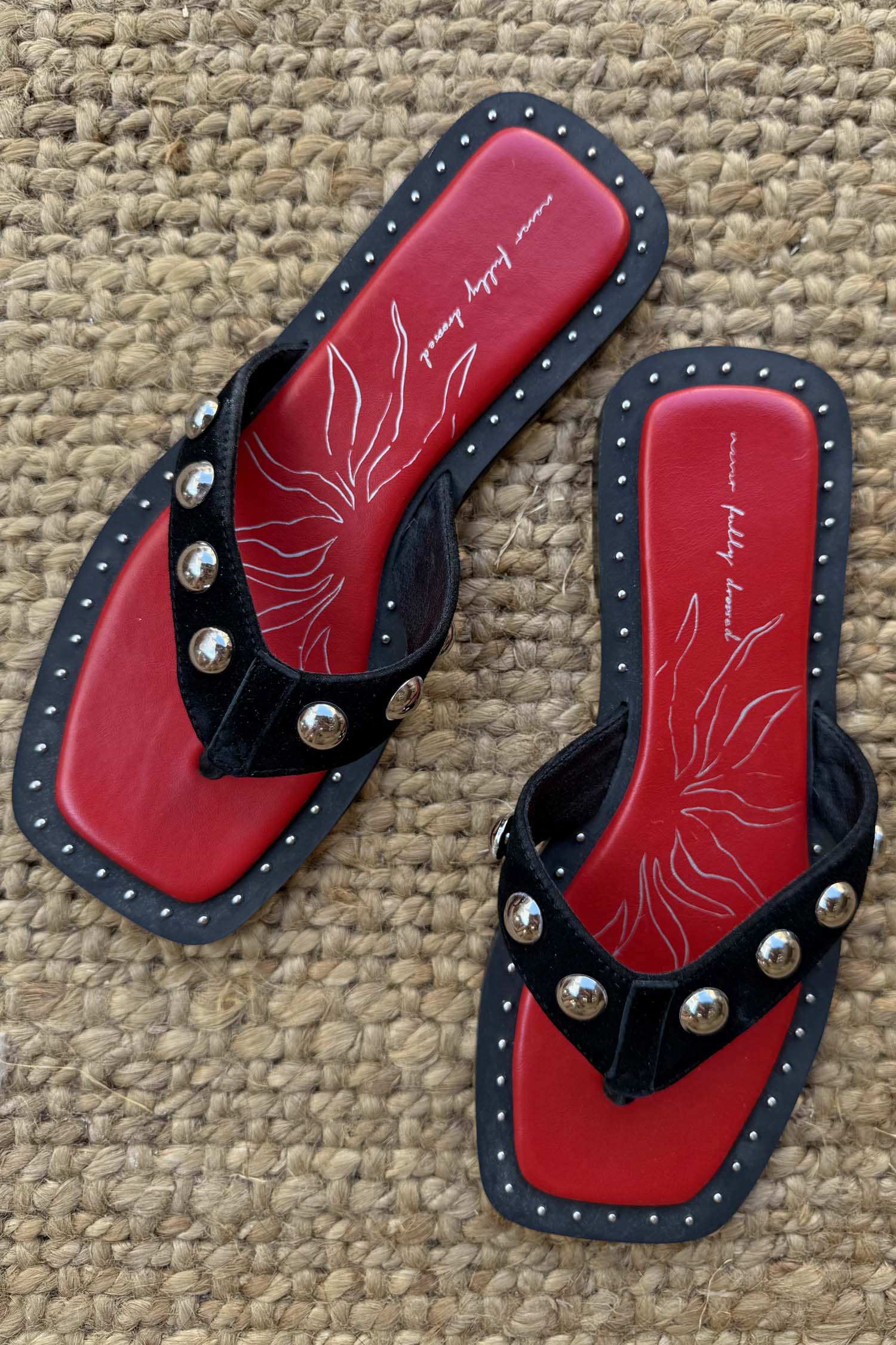 Black Leather Stud Sandals featuring a square toe, silver studs and a red footbed, displayed on a woven mat.