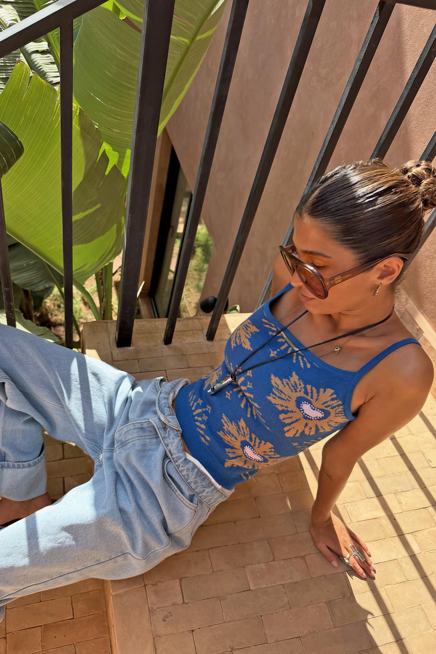Blue Eye Knitted Cami Top with woven eye and heart motifs, styled with light-wash jeans on outdoor stairs.