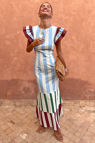 Blue Stripe Alena Midi Dress featuring ruffle sleeves and a multi-coloured tiered skirt against a textured wall.