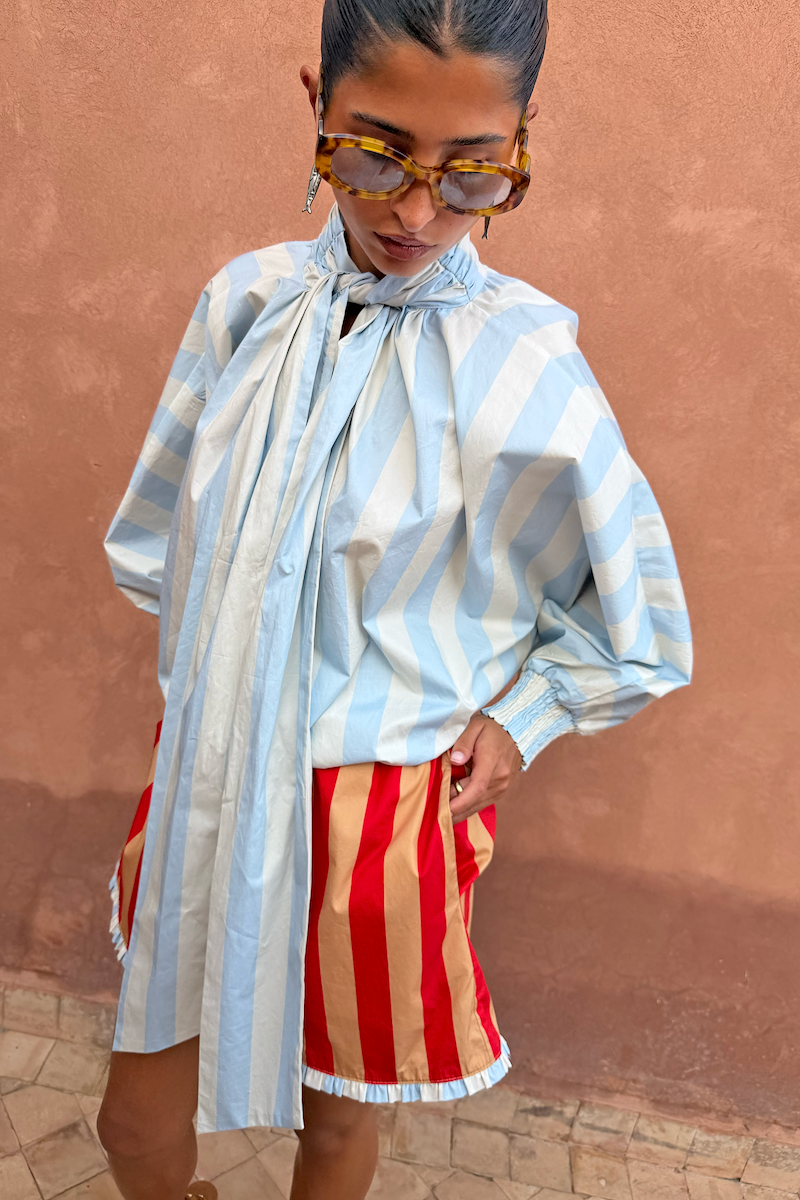 Blue Stripe Batwing Blouse with a high tie neck and voluminous sleeves, styled with red and tan striped shorts.