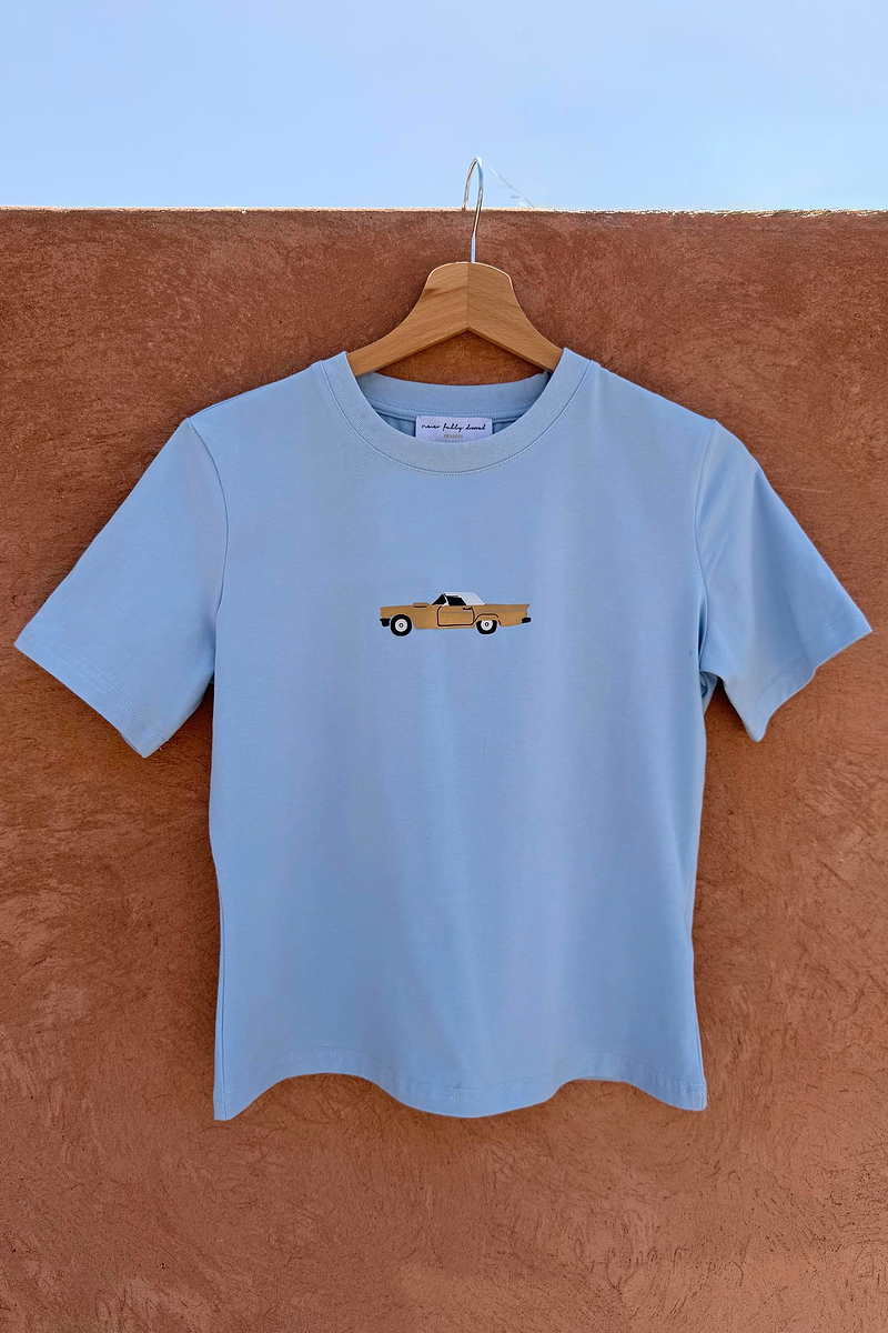 Cadillac Baby T-Shirt in blue stretch cotton with a retro car motif hanging on a wooden hanger.