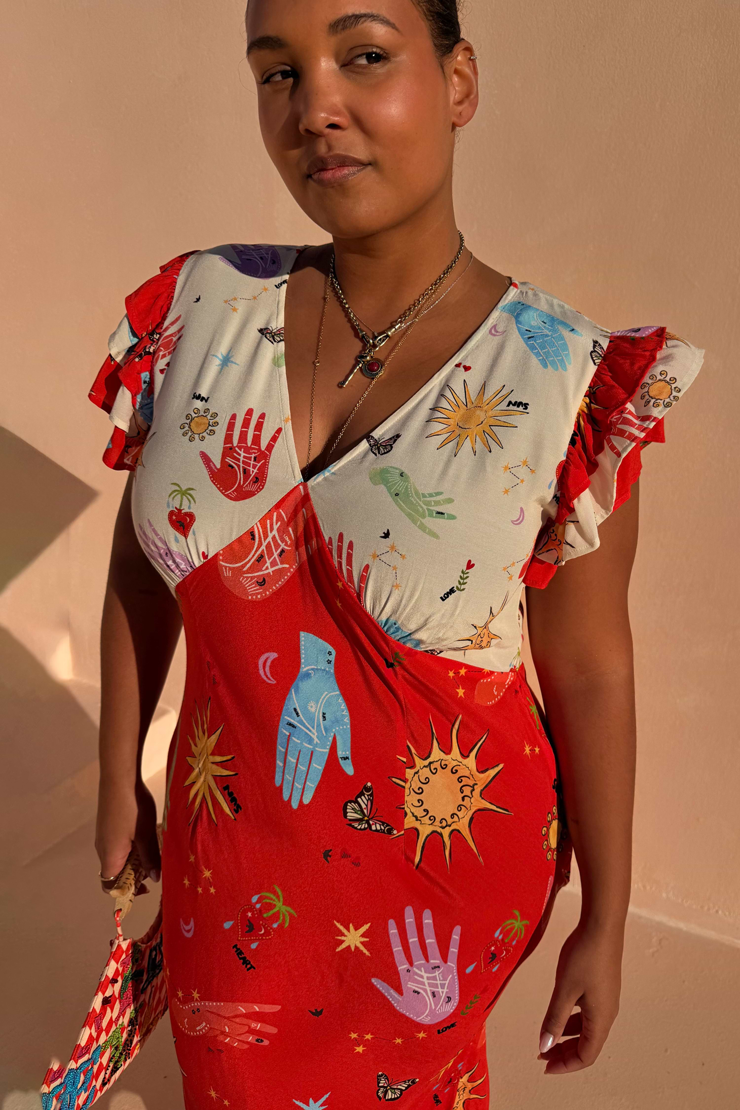 Red Celestial Midi Dress featuring a sun and hand print, V-neck blouson top and ruffled sleeves on a curve model.