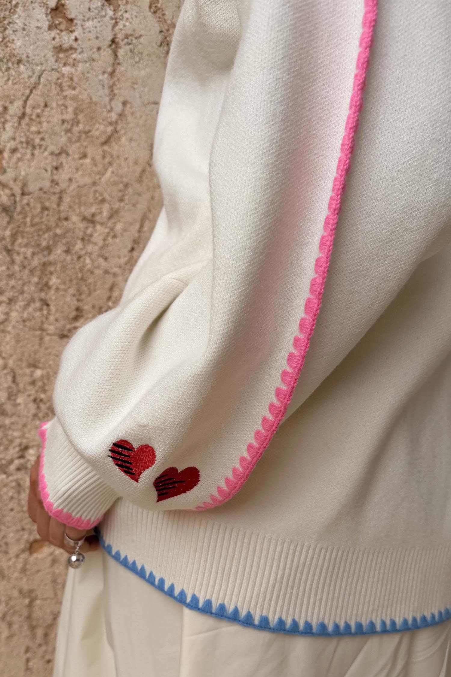 Cream Celestial Martha Cardigan detail highlighting the pink scalloped trim, red hearts and blue contrast hem.