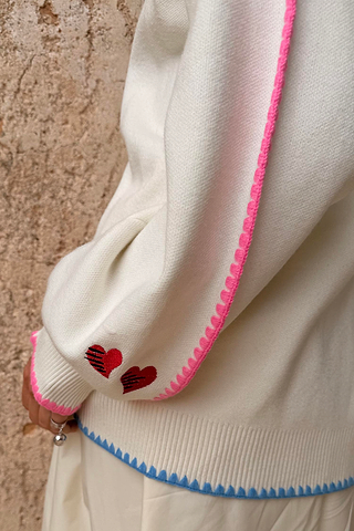 Cream Celestial Martha Cardigan detail highlighting the pink scalloped trim, red hearts and blue contrast hem.