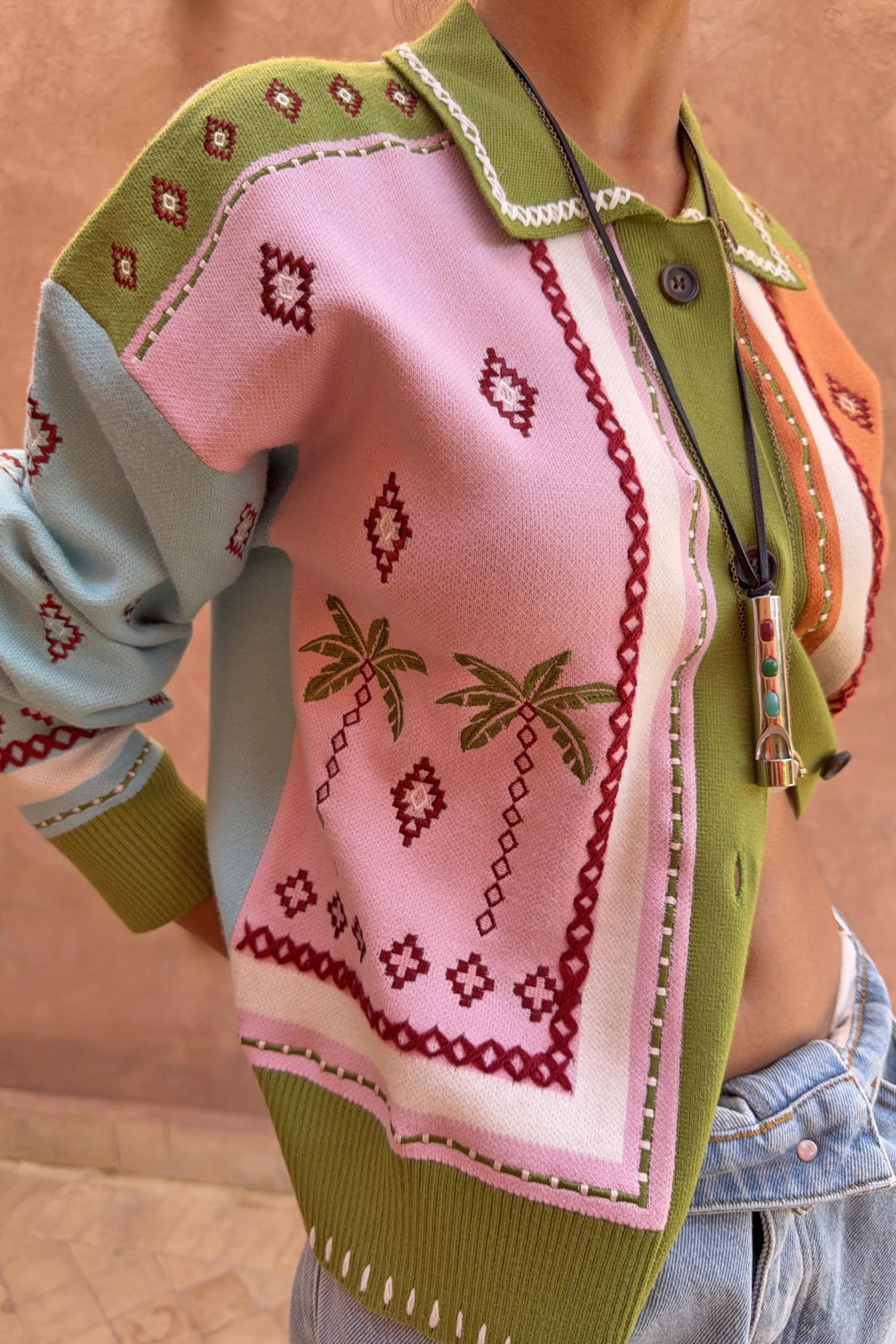 Green Geometric Palm Cardigan featuring pink jacquard panels, palm tree motifs and white blanket stitch trim.