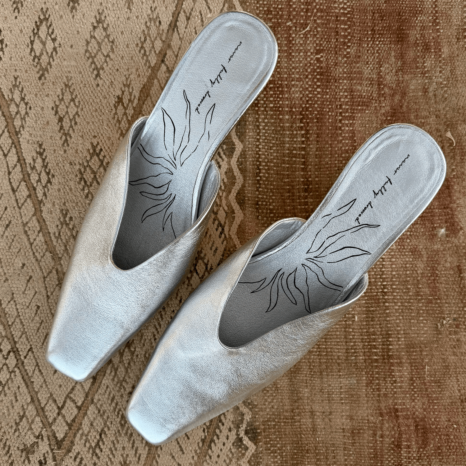Silver Wedge Mule in metallic real leather with a pointed toe and signature printed insole on a textured rug.
