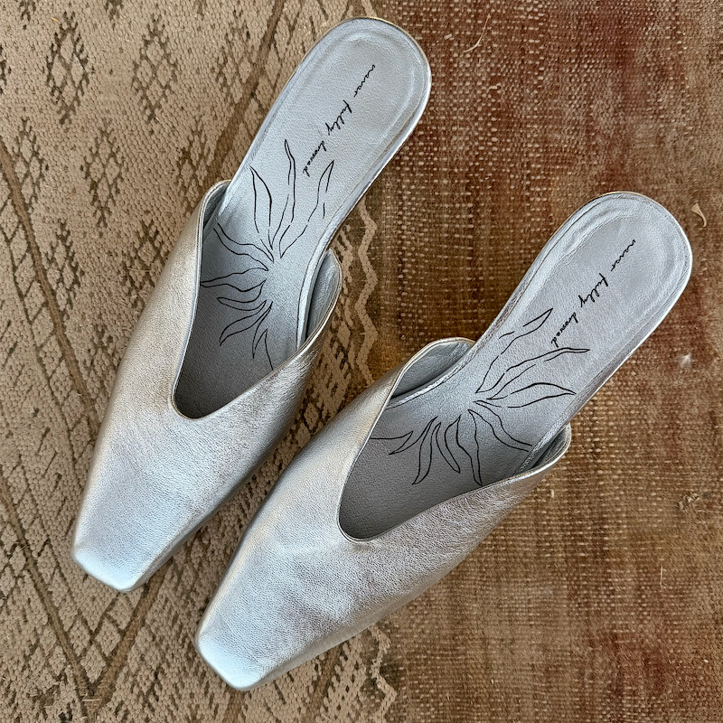 Silver Wedge Mule in metallic real leather with a pointed toe and signature printed insole on a textured rug.