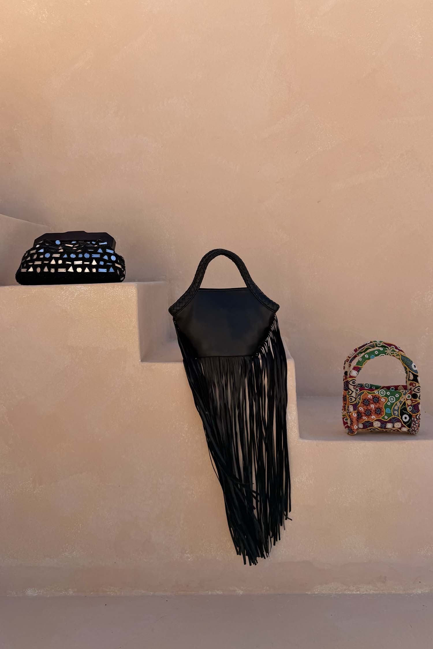 Black Leather Fringe Bag with long tassels and a plaited handle, styled on neutral steps with other bags.