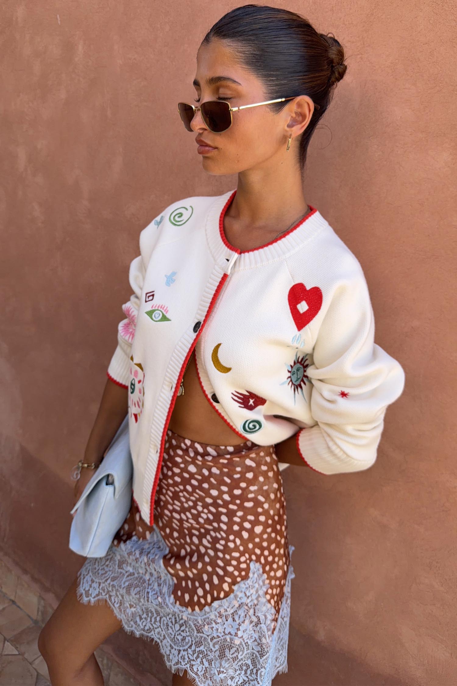 Cream Morocco Charms Cheryl Cardigan featuring red trim and embroidered motifs like hearts, palms and eyes.