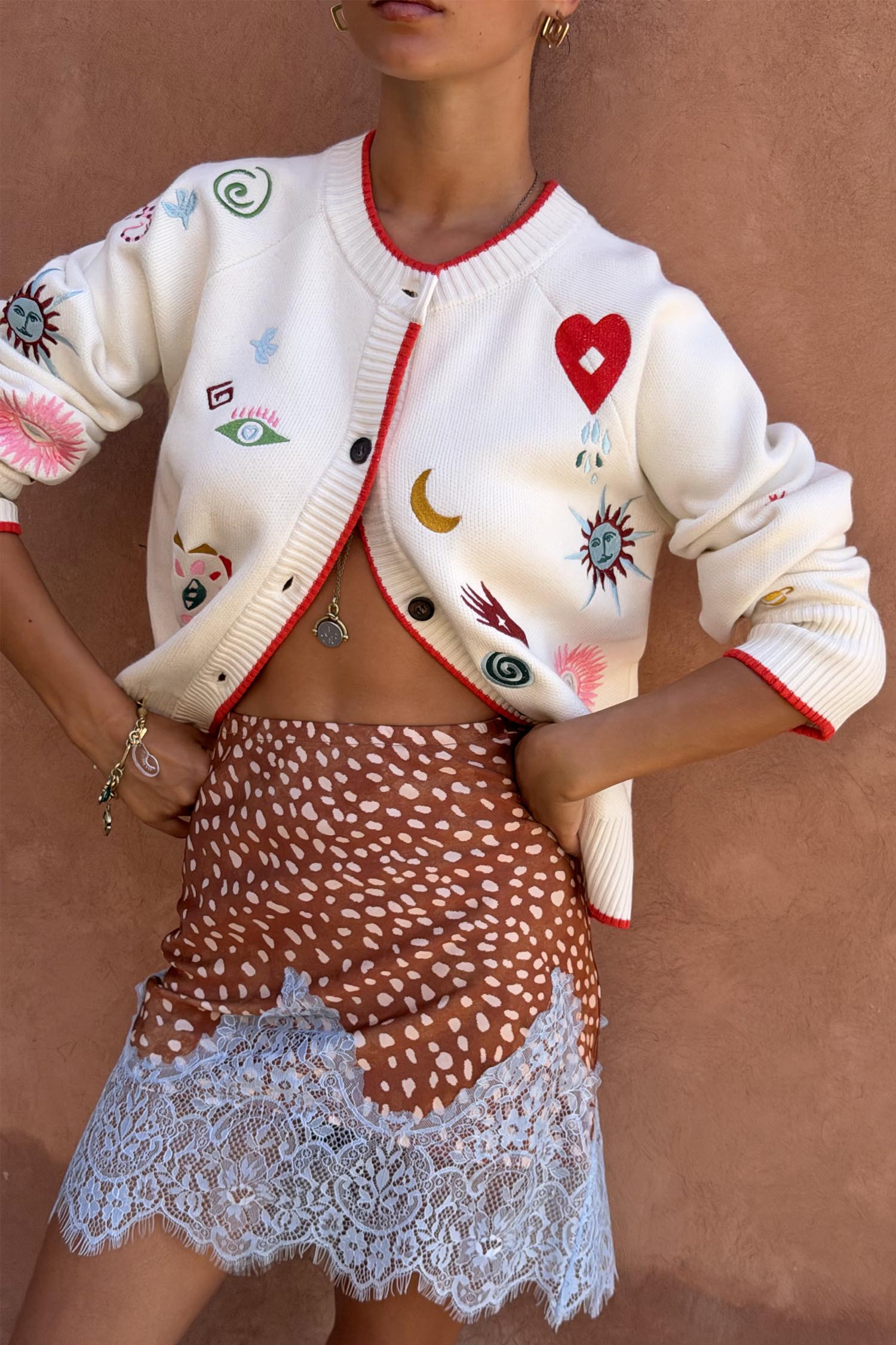Morocco Charms Cheryl Cardigan in cream with red trim and iconic motifs, paired with a leopard print lace-hem skirt.