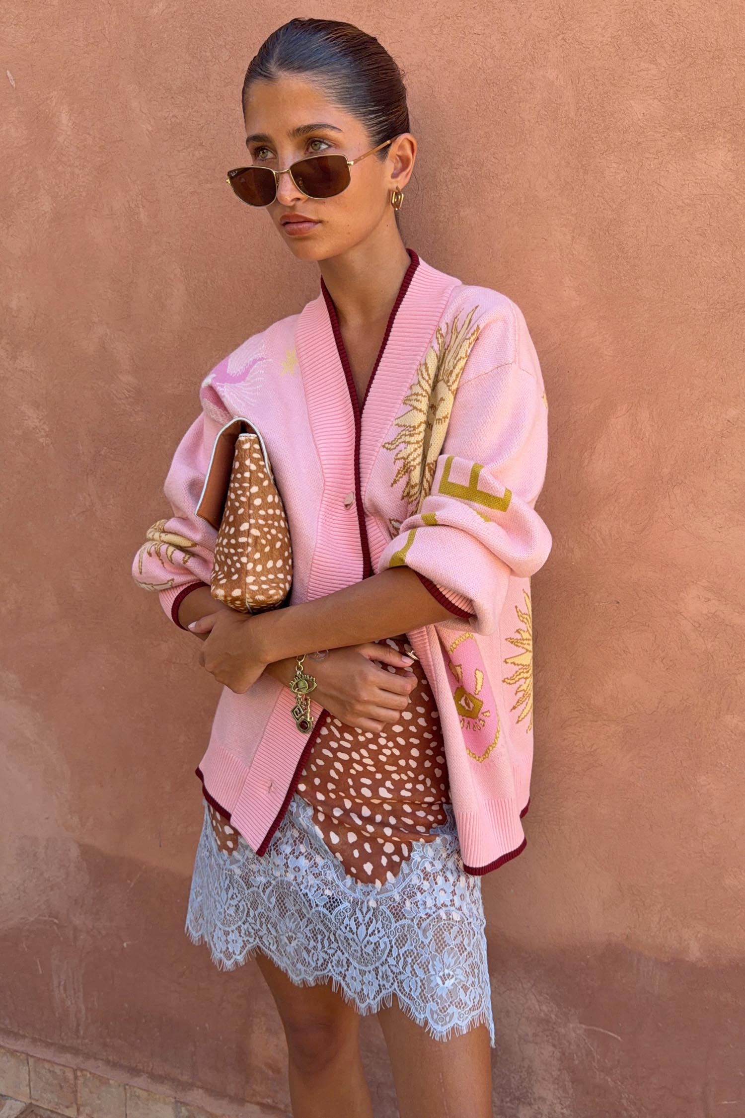 Pink Mystical Cardigan with jacquard sun and moon motifs and burgundy trims, styled with a lace-trimmed dress.