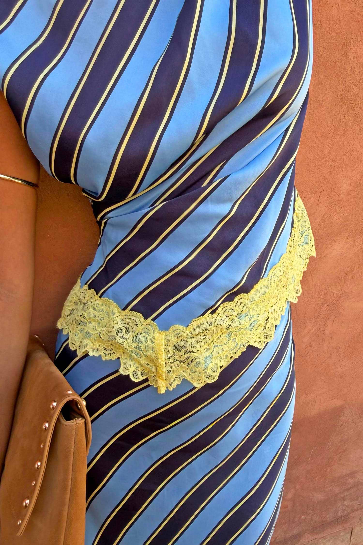 Stripe A-Symmetrical Top with blue and navy diagonal stripes and a yellow lace-trimmed hem, styled with a tan bag.