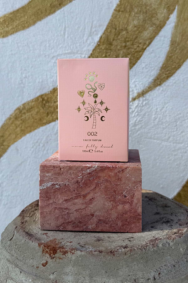 NFD Eau De Parfum 002 pink box with gold foil tropical icons, displayed on a pink marble block.