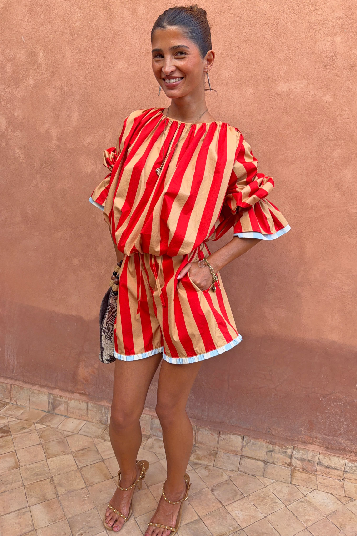 Model wearing the red and camel Tomato Stripe Blouse and matching shorts co-ord with voluminous sleeves and blue trim.