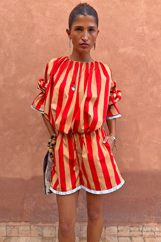 Tomato Stripe Ellie Shorts in red and camel cotton co-ord with contrast hem trim against a textured wall.