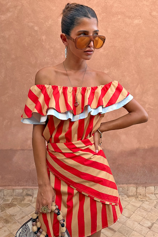 Tomato Stripe Scarf in red and tan styled as a multi-wear ruffled top against a terracotta wall.