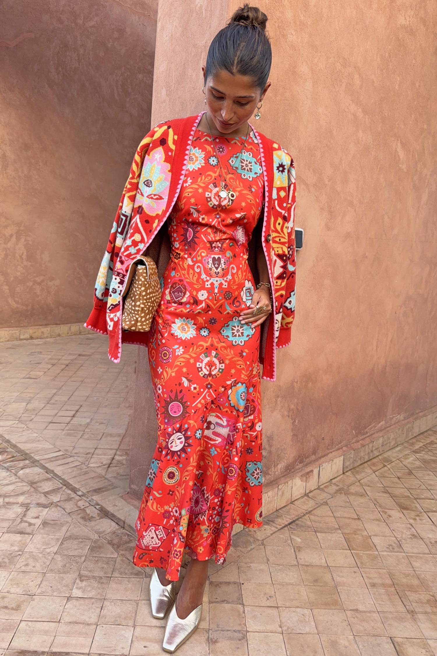 Tomato Tapestry Frida Dress in red with sun motifs, layered with a coordinating cardigan and metallic shoes.