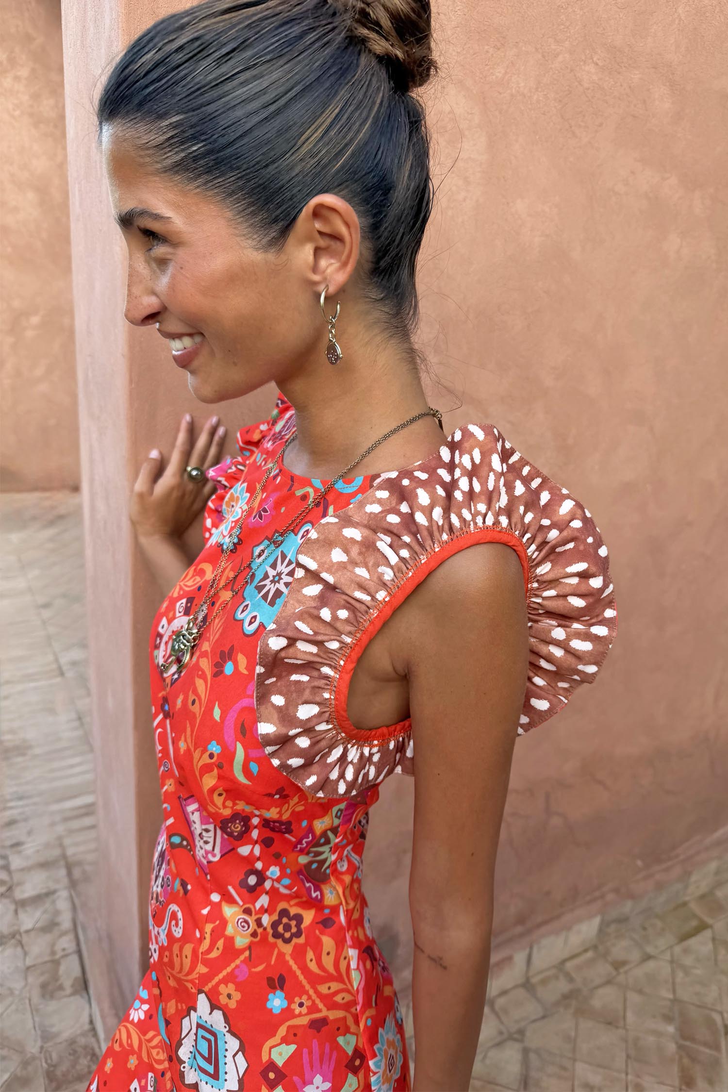 NFD Tomato Tapestry Frida Dress in red with sun motifs, florals and contrasting spot print frill sleeves on a model.