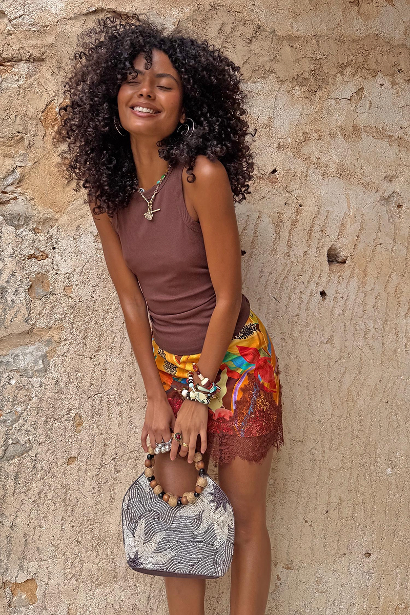 Chocolate Ribbed Tank styled with a colourful floral skirt and beaded bag against a stone wall.