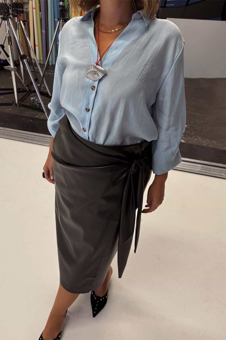 Black vegan leather Jaspre wrap midi skirt with a tulip tie on a UK size 18 model, with a light blue shirt.