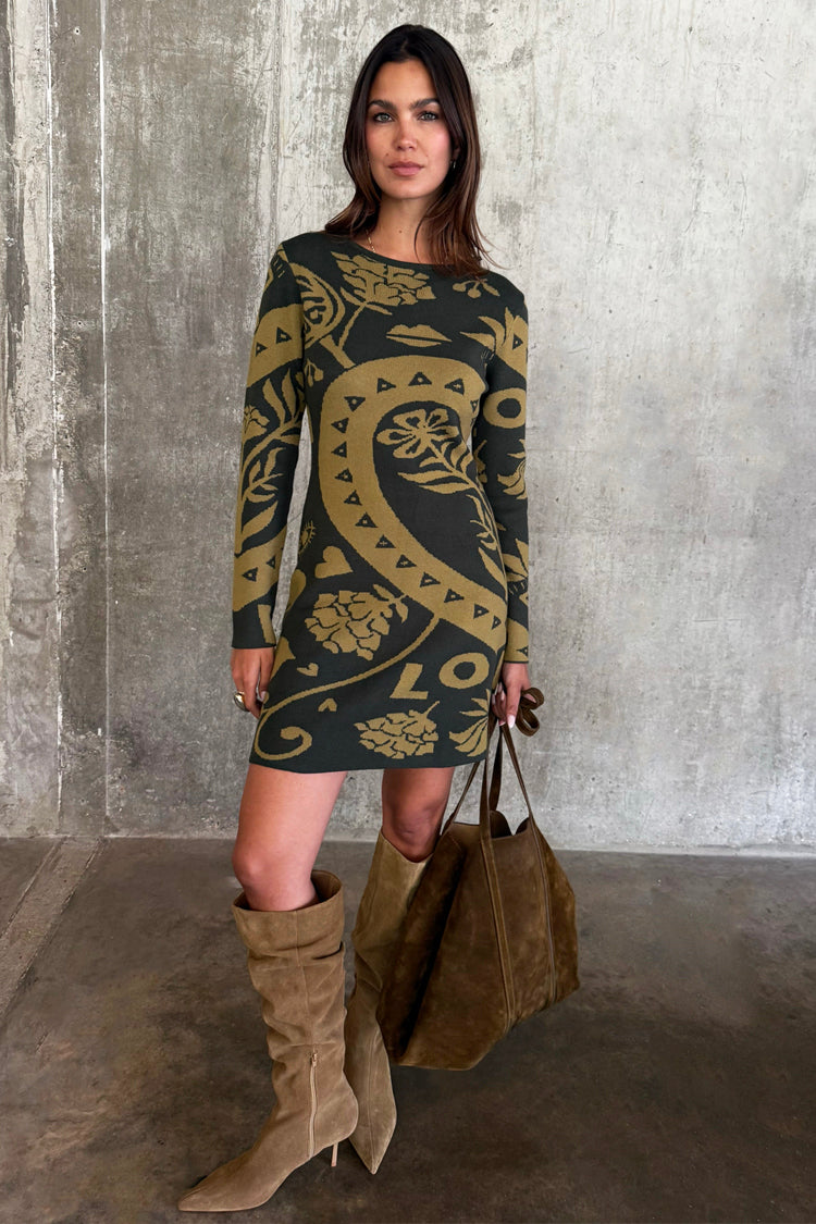 Olive Amara Knit Mini Dress with iconic hand, flower and eye motifs, styled with tall suede boots and a brown tote bag.