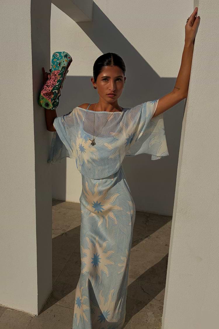 Blue Soleil Anais Dress featuring sun motifs, a sheer draped top, and a flowing satin-esque skirt.