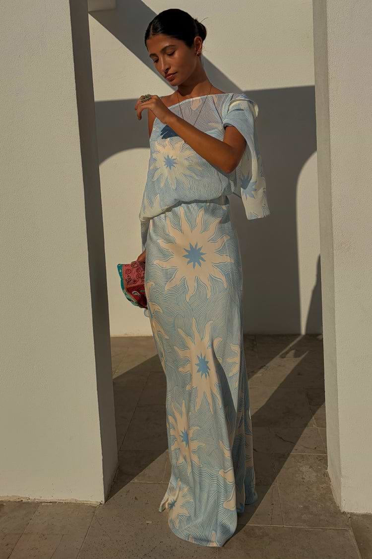 NFD Blue Soleil Anais Dress with a Mediterranean sun print, featuring a draped off-the-shoulder top and flowing skirt.