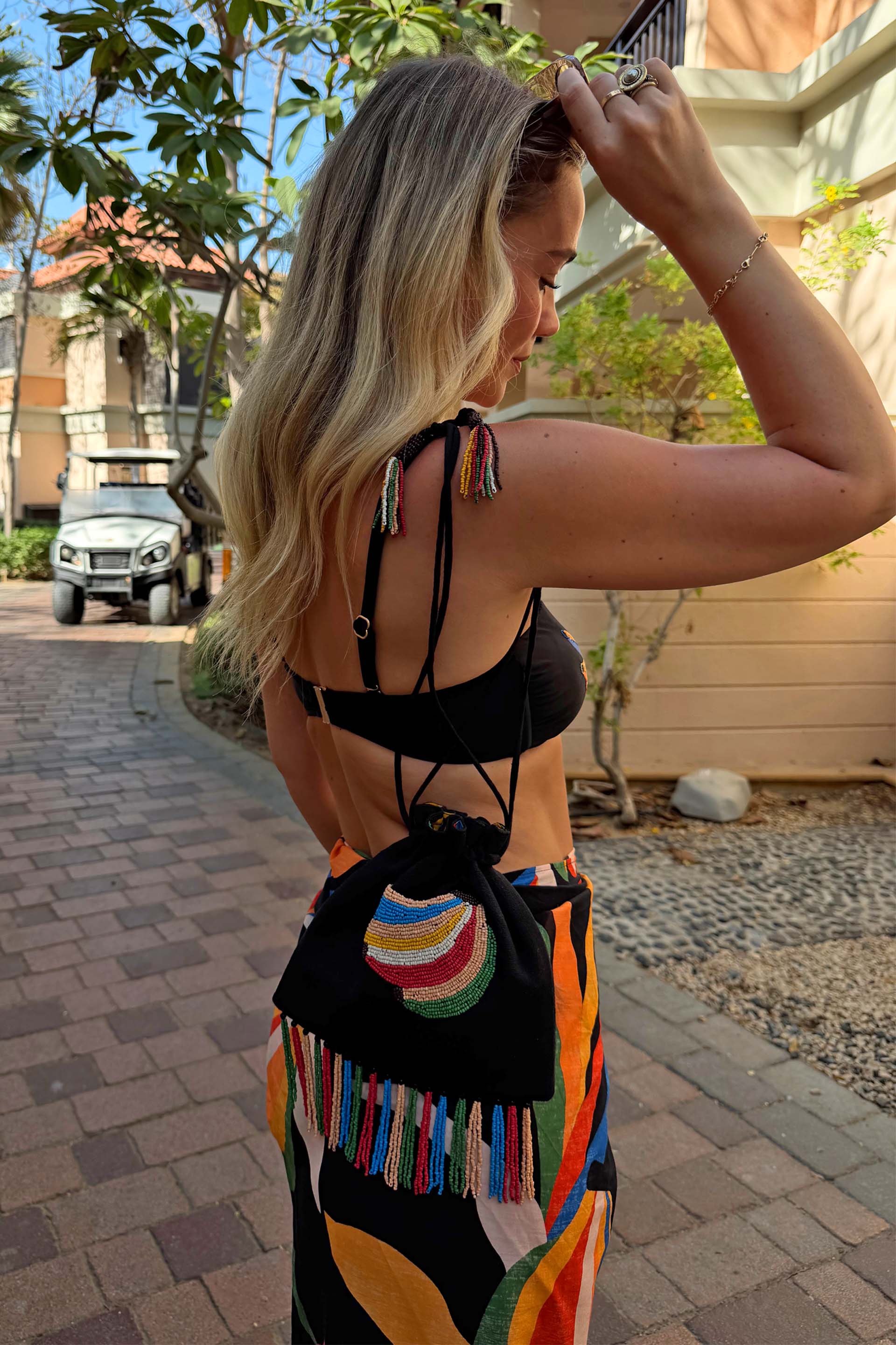 Black Banana Pouch Bag featuring a beaded banana motif and multicolour fringe, styled with a vibrant printed sarong.
