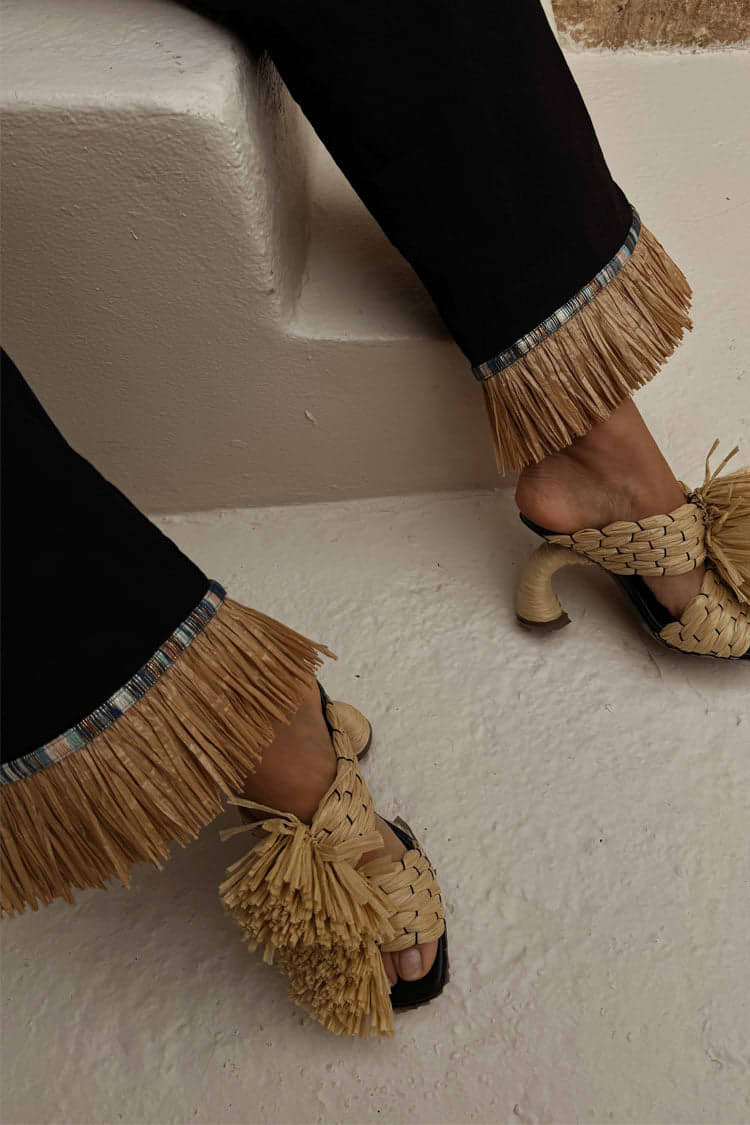 Black Raffia Marra Trousers featuring fringe hems, styled with woven raffia heels on white steps.