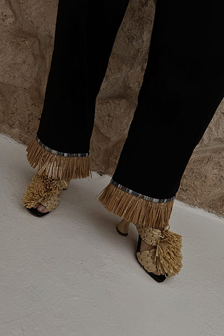 Black Raffia Marra Trousers featuring tan raffia fringe at the hem, styled with woven raffia sandals.