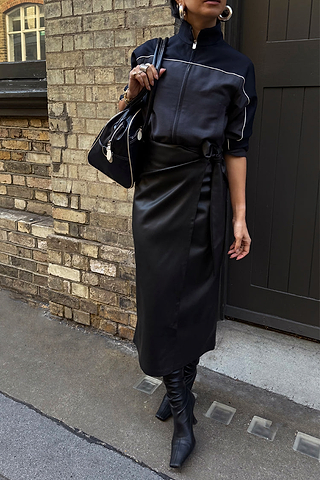 Black Vegan Leather Jaspre Wrap Skirt with a tulip tie, styled with a black zip jacket and boots.