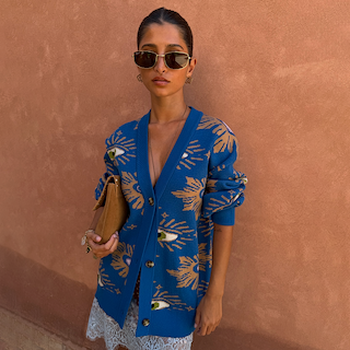 Relaxed fit Blue Eye Cardigan with iconic eye motifs, layered over a lace slip dress and tan clutch.