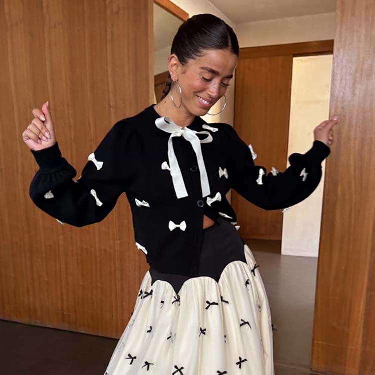 Black Bow Sophie Cardigan in a heavy knit with cream 3D bows and a tie neck fastening, worn by a smiling model.