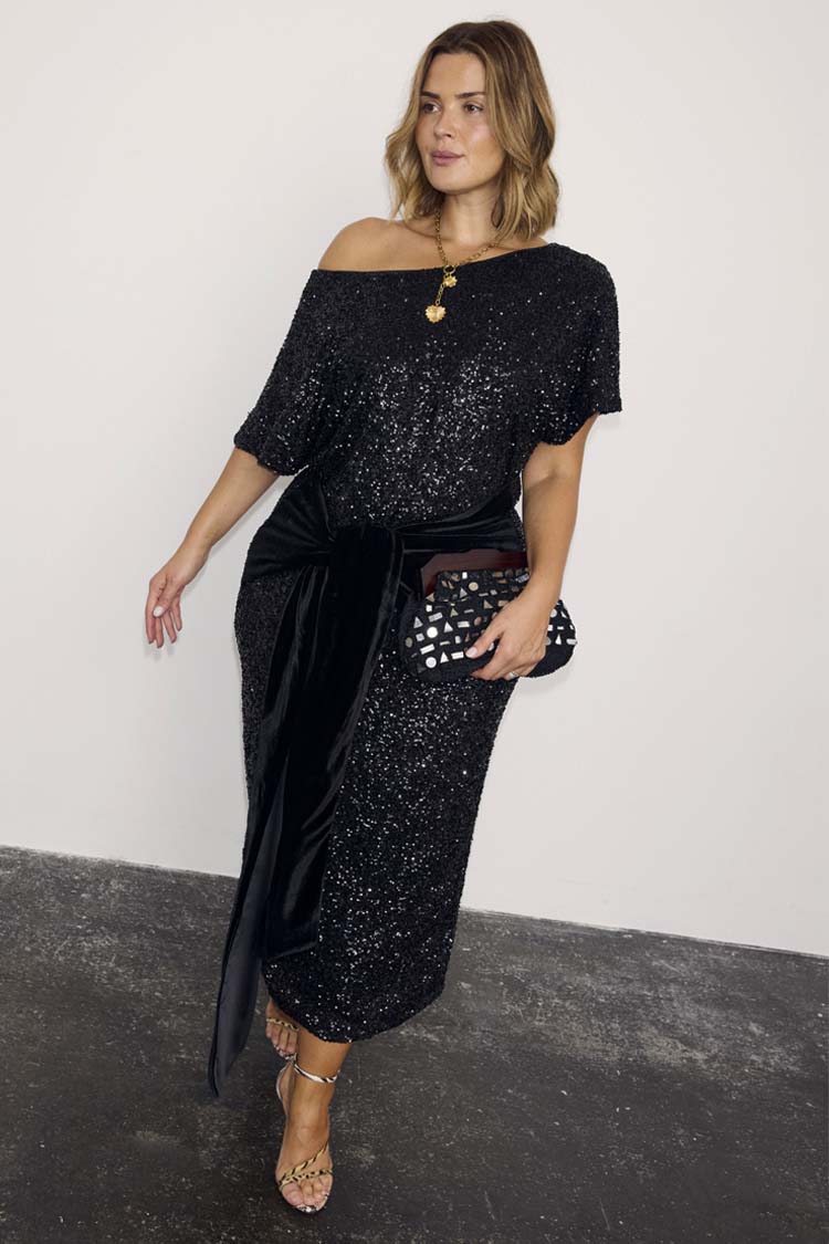 Black Sequin Bow Dress in a shimmering midi length with a velvet waist tie, styled with a patterned clutch bag.