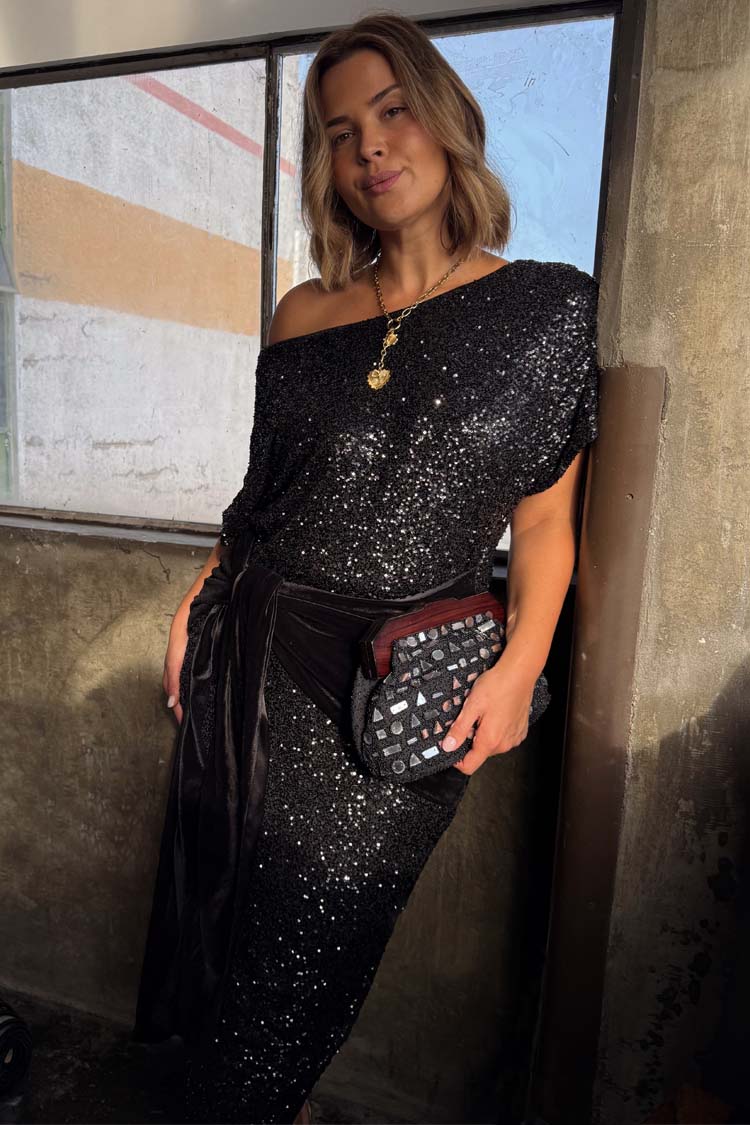 Black Sequin Bow Midi Dress styled off-the-shoulder with a velvet multi-wear tie, shown on a model with a clutch.