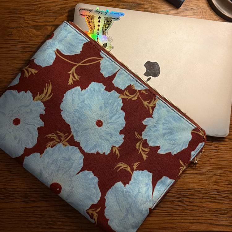 Blue and Burgundy Poppy Laptop Case with a large floral print and zip closure, holding a silver laptop on a wooden desk.