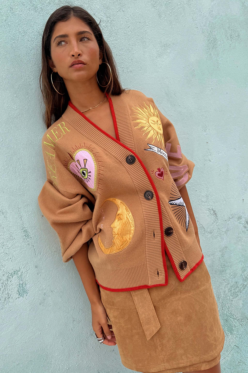 Model wears Camel Mystical Cardigan with gold sun and moon embroidery and red ribbed trim.