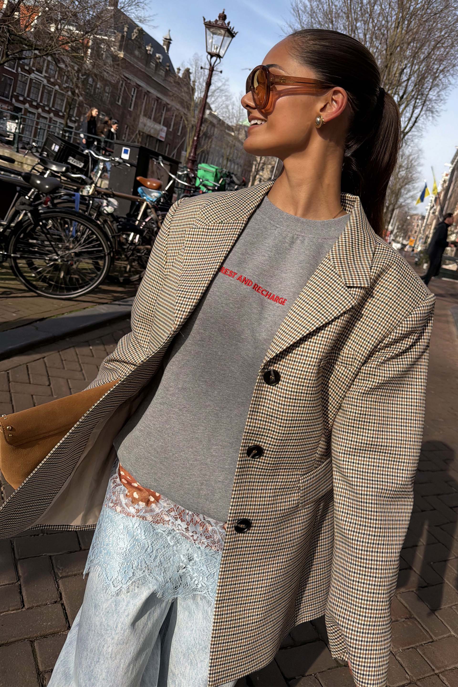 Grey tailored Check Blazer with button detailing and structured darts, styled over a grey slogan sweatshirt in an outdoor setting.