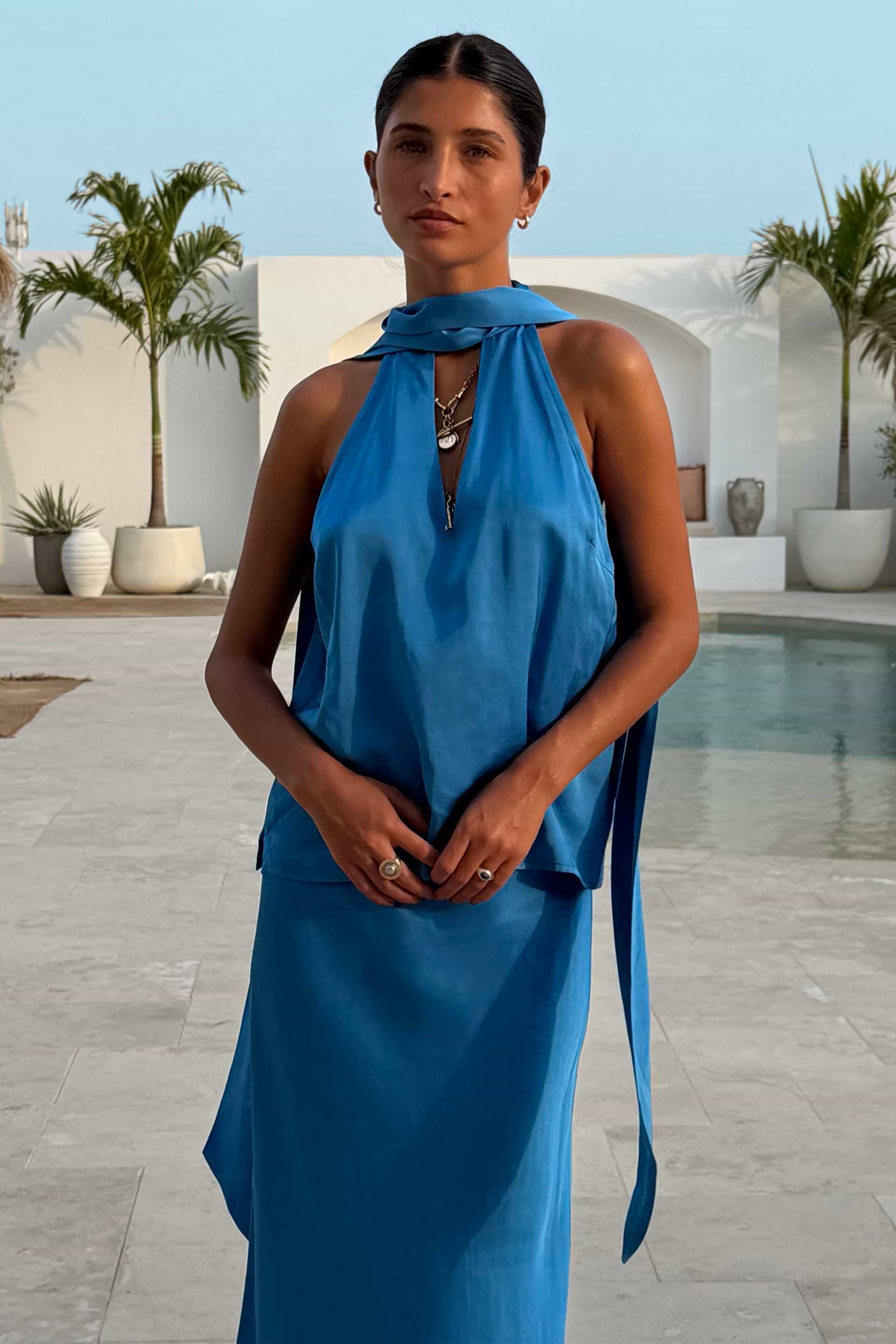 Cobalt Lily Top in blue satin-feel fabric with multi-wear tie neck fastenings, styled as a co-ord by a pool.