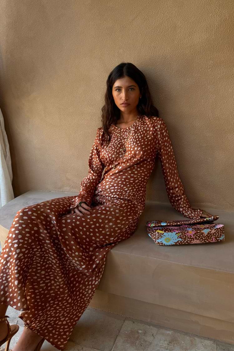 Fawn Soho Dress in brown satin-esque deer print with long sleeves, shown on a seated model with a printed clutch.