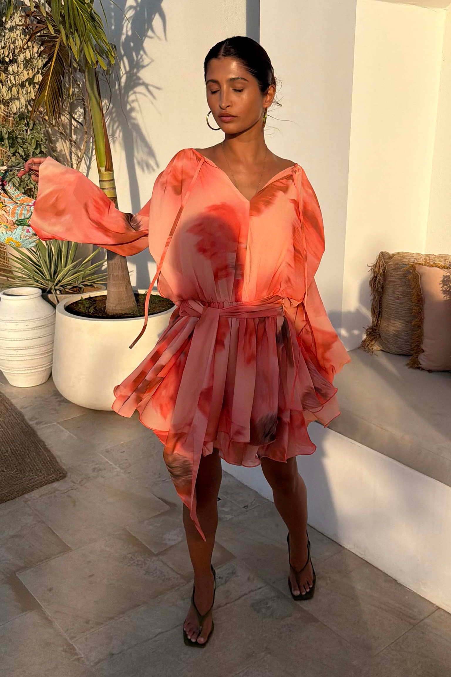 Blurred Floral Ella Mini Dress in peach orange with tiered ruffles and flute sleeves, styled outdoors.