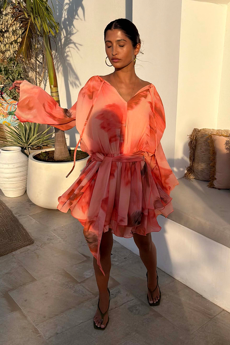 Blurred Floral Ella Mini Dress in peach orange with tiered ruffles and flute sleeves, styled outdoors.