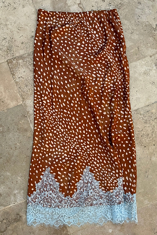 Fawn Midi Maeva Skirt Petite in a brown spotted print with a pale blue lace trim on a stone background.