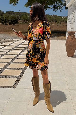 Black Sofia Mini Tea Dress with an orange and pink floral print and frill hem, styled with tan fringe boots.
