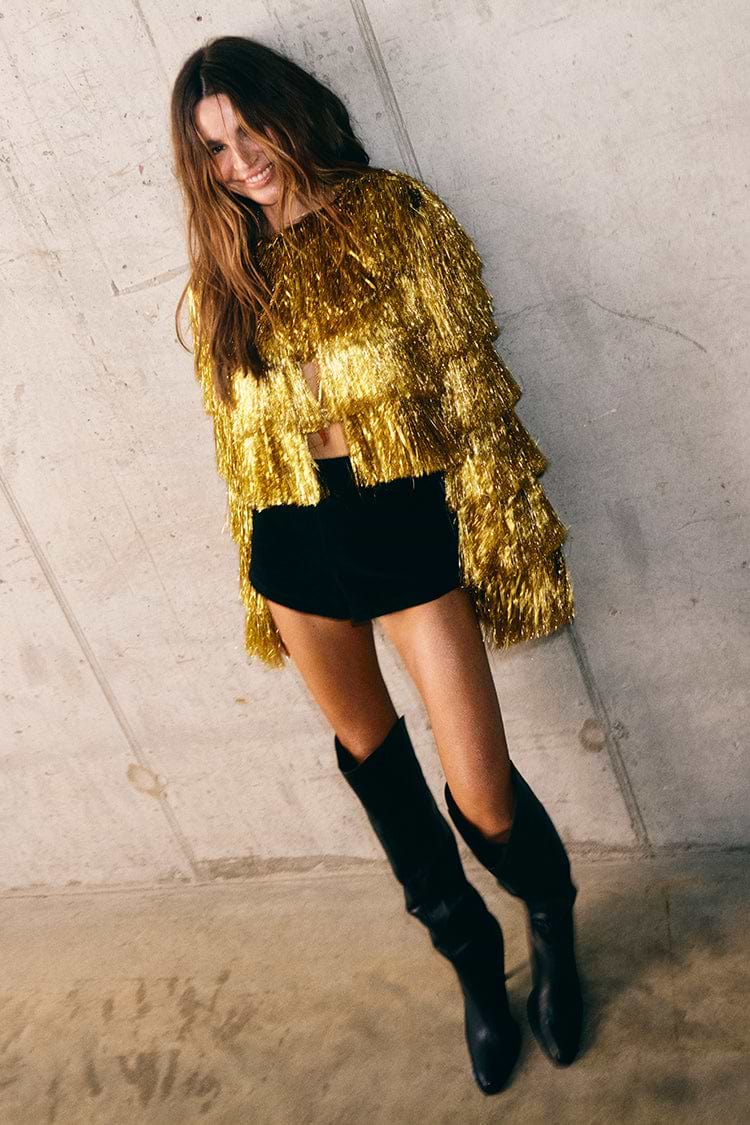 Gold Fringe Jacket with tiered gold foil tassels, styled with black shorts and tall black boots.