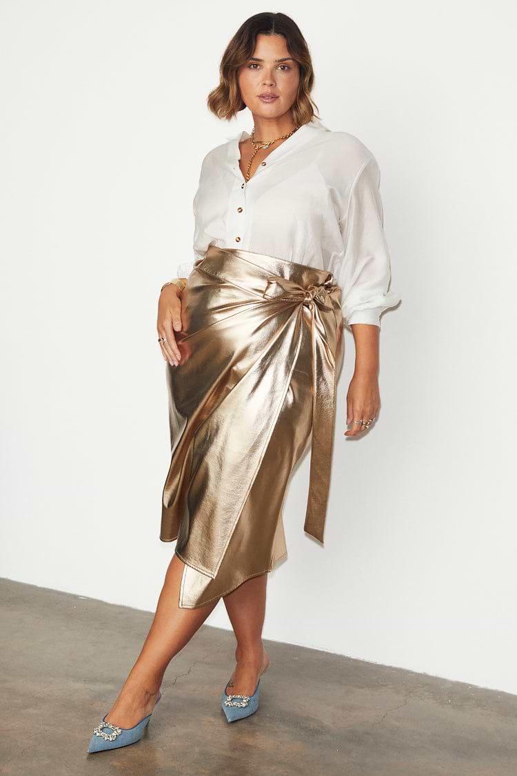Gold vegan leather Jaspre wrap skirt styled with a white button-down shirt and blue heels.
